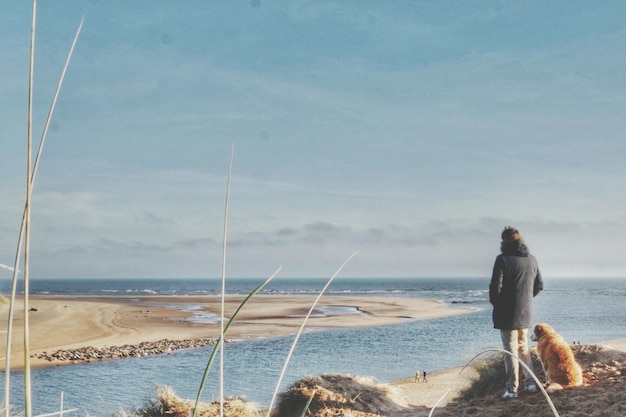 사진 하늘을 배경으로 해변을 바라보는 개와 함께 서 있는 여자
