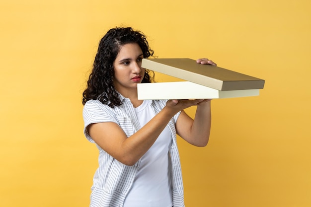 Woman standing with gift box in hands looking inside and does not like her present for birthday