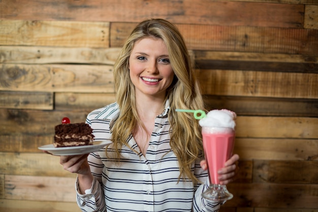 Woman standing with glass of milkshake and pastry in coffee