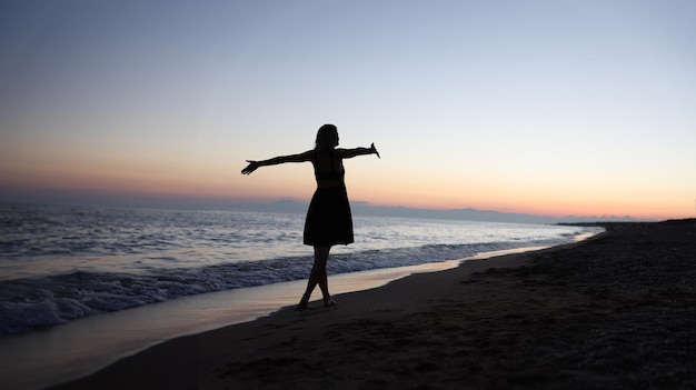 Woman standing with open arms on seashore at sunset