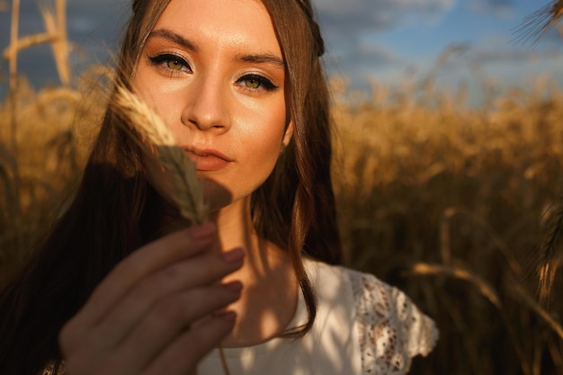 フィールドで小麦の小穂と立って、カメラを見ている女性