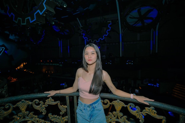 A woman stands on a balcony in front of a black and blue neon light.