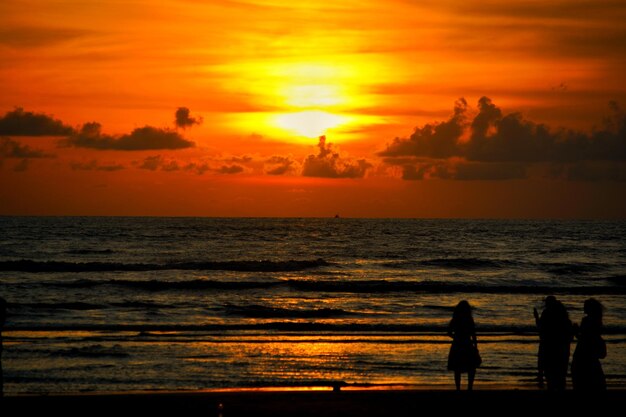 A woman stands on the beach in front of a sunset