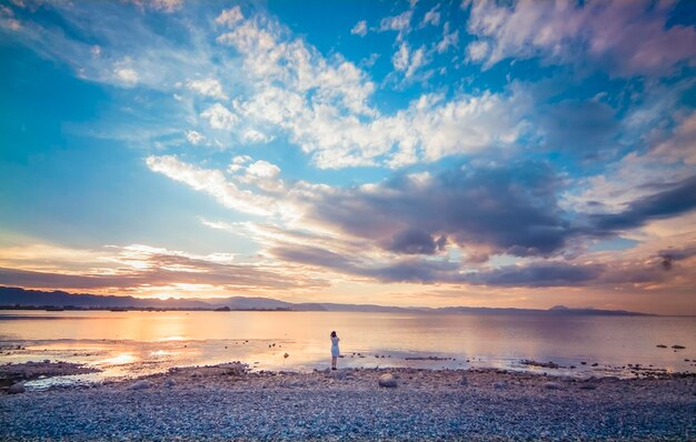 Photo a woman stands on a beach at sunset with a cloudy sky behind her.