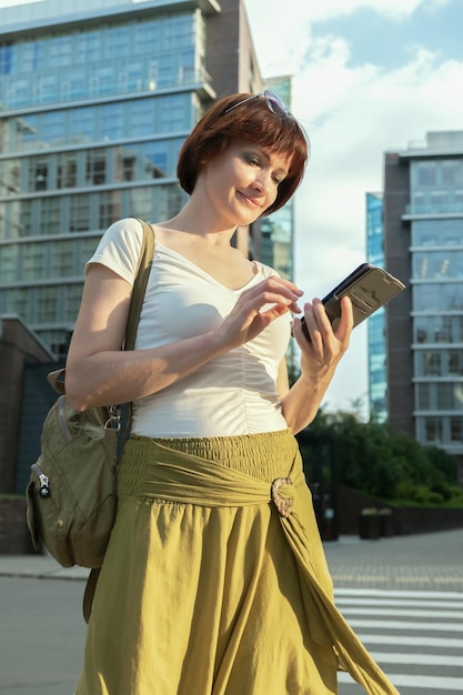 Woman stands in a business city district and looks at the screen of smartphone