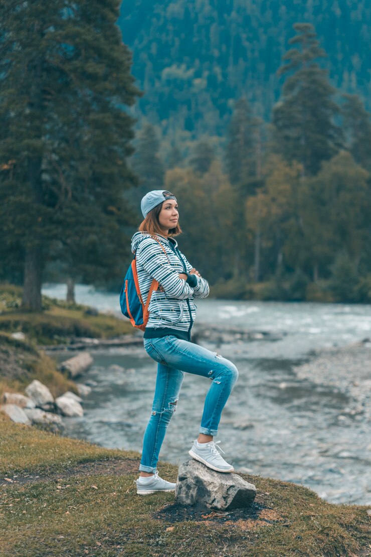 女性が川のそばに立ち、山を眺めている。山麓でのハイキング。