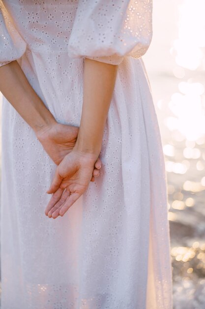 Woman stands by the sparkling sea with her hands behind her back Cropped Faceless Back view