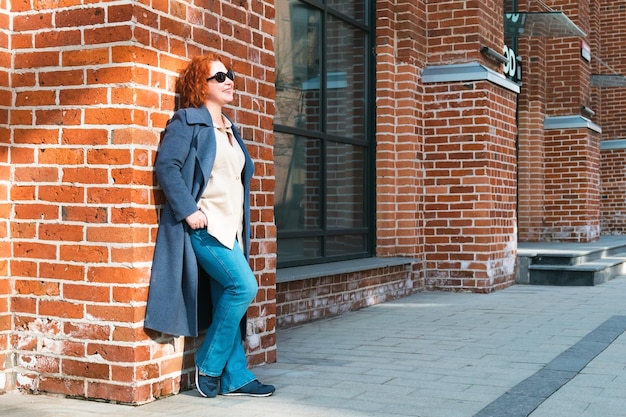 A woman stands in front of a brick wall with the word cafe on it.