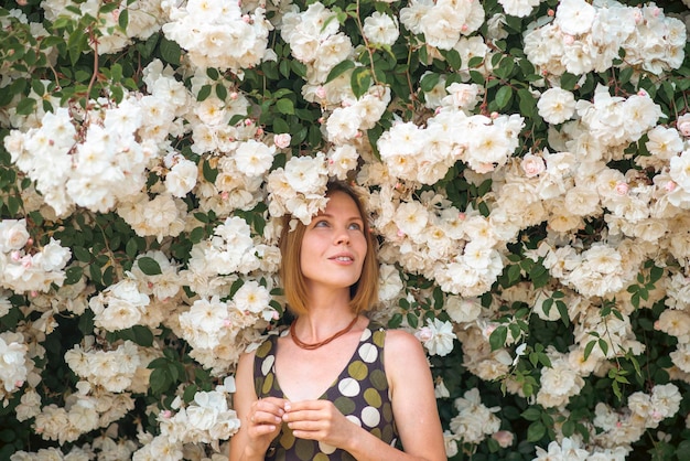 A woman stands in front of a large bush of flowers.