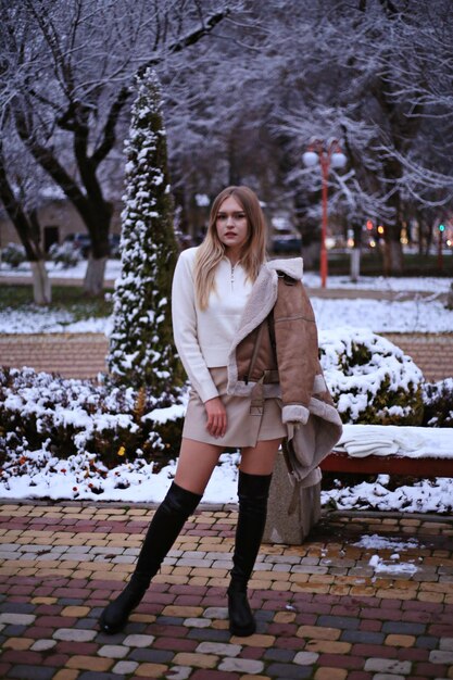 a woman stands in front of a snow covered park bench