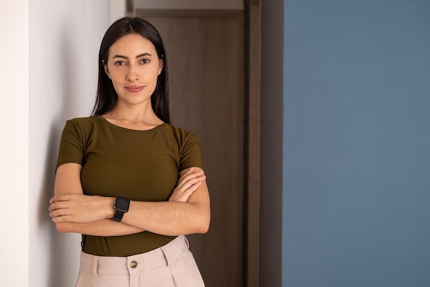 A woman stands in front of a wall with her arms crossed.