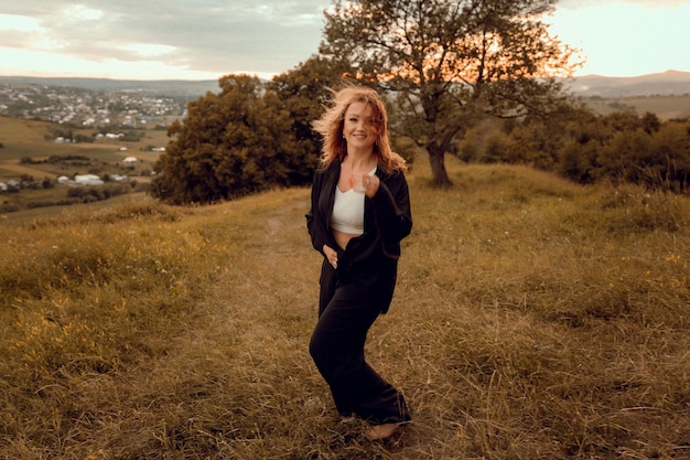 A woman stands on a hill in a field with a tree in the background