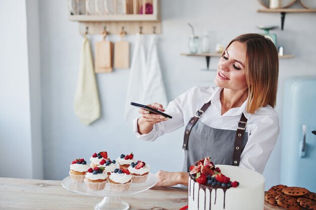 Woman stands in the kitchen and takes photo of her homemade cookies and pie by using phone.