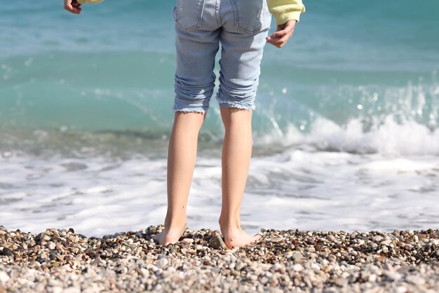 Woman stands on line of sea surf on sunny day cropped image of female legs and sea with waves