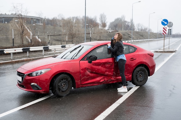 Женщина стоит возле разбитой машины после аварии. звать на помощь. страхование автомобиля