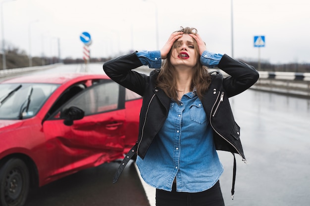 Woman stands near a broken car after an accident