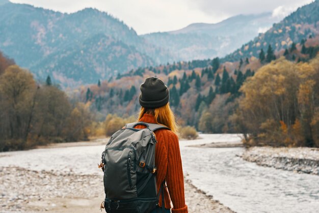 Woman stands on the river bank and looks at the mountains in the distance landscape autumn backpack tourism model