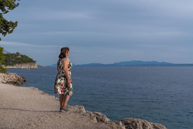 Женщина стоит на берегу моря и смотрит вдаль перед закатом