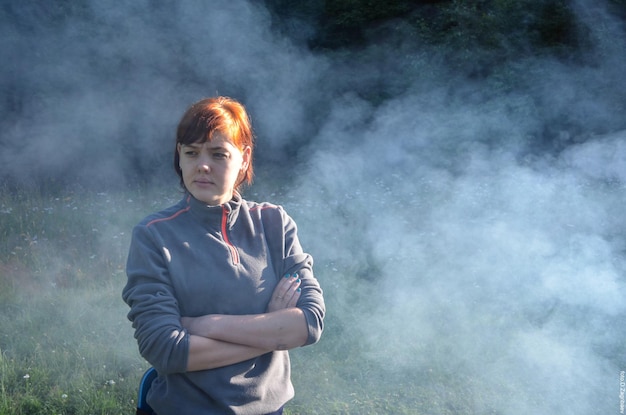 A woman stands in smoke with her arms crossed