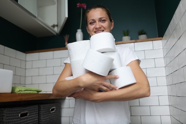 Photo woman stands in toilet and holds stack of toilet paper rolls in her hands.