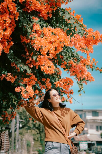 オレンジ色の花を背景に木の下に立っている女性。