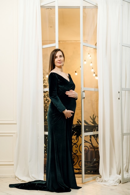 woman stands in a velvet evening dress near the window