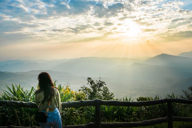 A woman stands to watch the view and the sun rise in the morning sky.