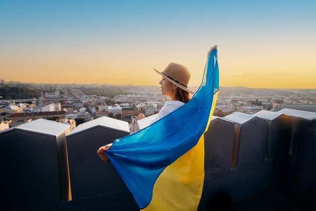 a woman stands with the national ukrainian flag and waving it praying for peace at sunset in lvivxaa symbol of the ukrainian people independence and strength pray for ukraine