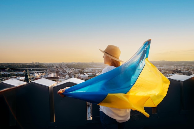 A woman stands with the national Ukrainian flag and waving it praying for peace at sunset in LvivxAA symbol of the Ukrainian people independence and strength Pray for Ukraine