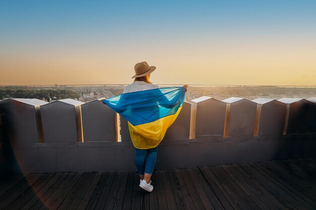 a woman stands with the national ukrainian flag and waving it praying for peace at sunset in lvivxaa symbol of the ukrainian people independence and strength pray for ukraine