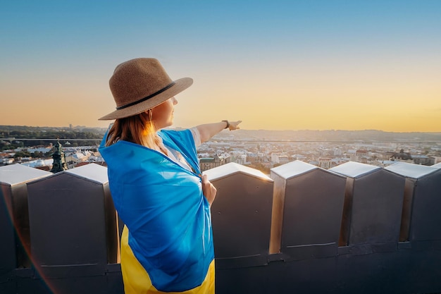 女性は、ウクライナの国旗を掲げて立って、ウクライナの人々の独立と強さの象徴であるLvivxAAで、日没時に平和を祈って手を振っています。ウクライナのために祈る