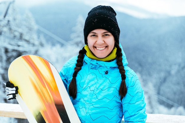 woman stands with snowboard on the top of the snowed hill