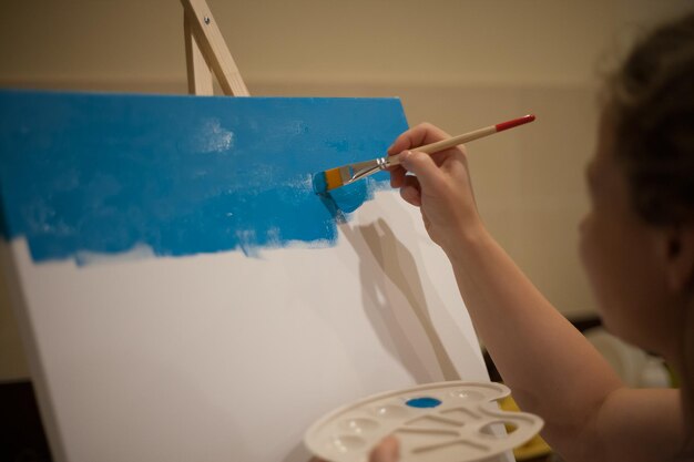 Женщина начинает рисовать синим акрилом, рисует белую рамку для холста.