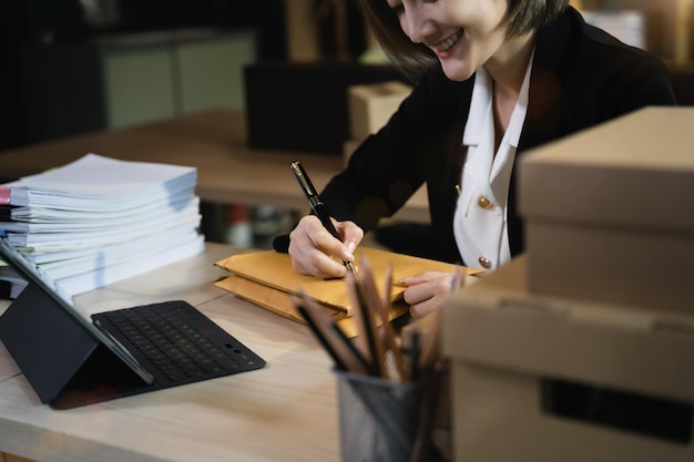 Woman start up small business owner writing address on cardboard box at workplacesmall business entrepreneur SME or freelance asian woman working with box at home Shipping shopping online