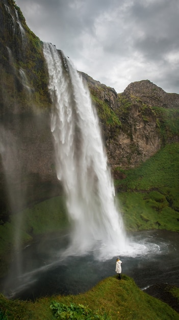 女性はアイスランドの滝にとどまるアイスランドの滝を隠す