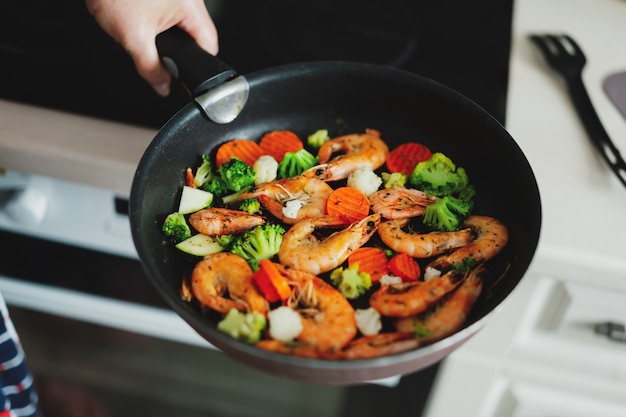 Woman staying at home kitchen and cooking shrimps with vegetables on pan. Home cooking or healthy cooking concept