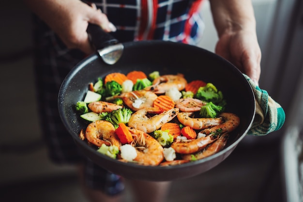 Woman staying at home kitchen and cooking shrimps with vegetables on pan. Home cooking or healthy cooking concept