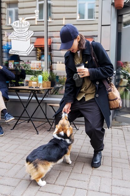 A woman stays and plays with corgi dog on an outdoor veranda at a table in blue cap