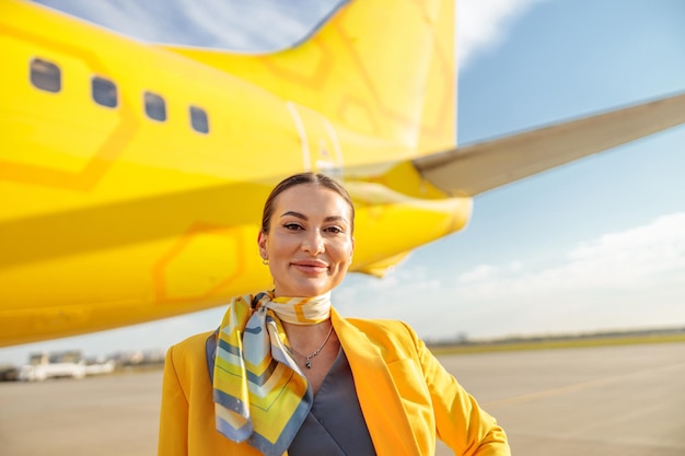 Woman stewardess or air hostess looking at camera and smiling while standing outdoors at airport