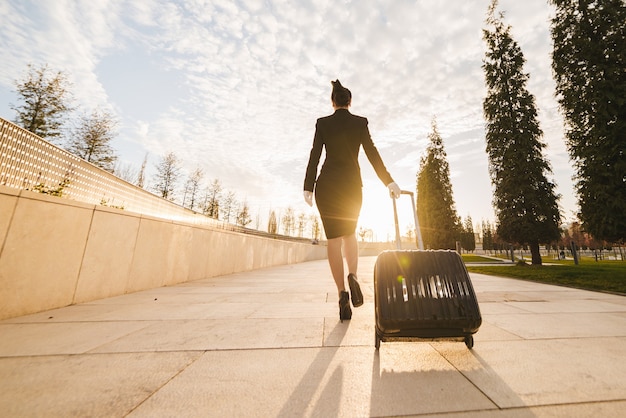 青い空を背景に制服を着た女性スチュワーデスは大きなスーツケースを運ぶ