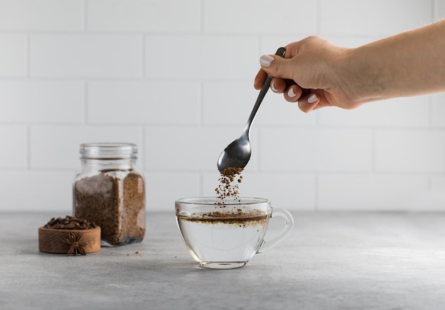 Photo woman stirs instant coffee in glass mug with boiled water on grey stone table