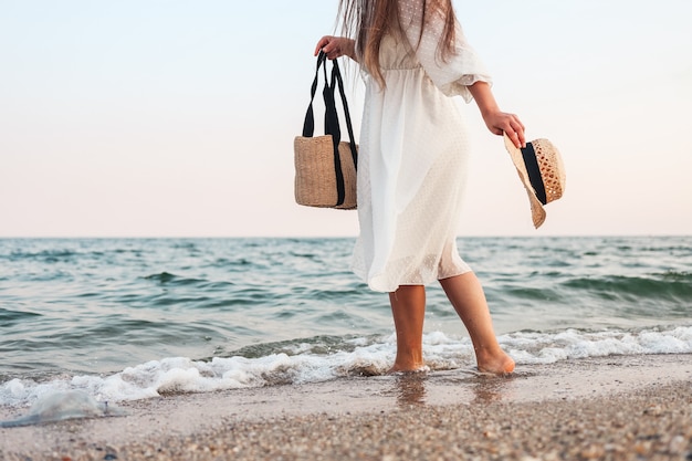 茶色のバッグと熱帯のビーチで麦わら帽子と白いドレスの女性。
