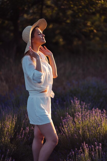 Женщина в соломенной шляпе в белом костюме из легкой ткани на сиреневом поле