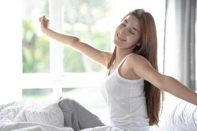 Woman stretching in bed after wake up in the morning on big window background in bedroom