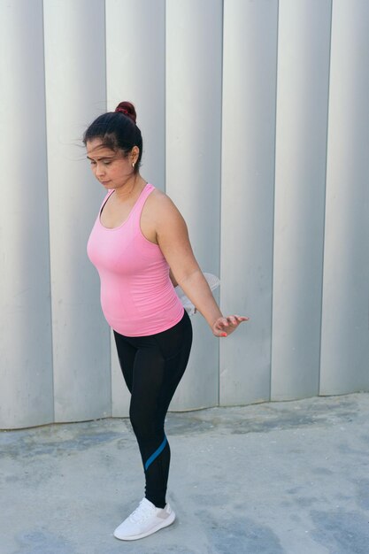 Woman stretching her leg in sportswear looking away during workout on city street.