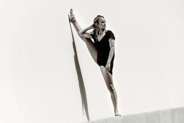 Photo woman stretching legs against wall in sunny day