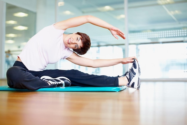 Donna che allunga ritratto di donna sorridente facendo un esercizio di stretching in palestra