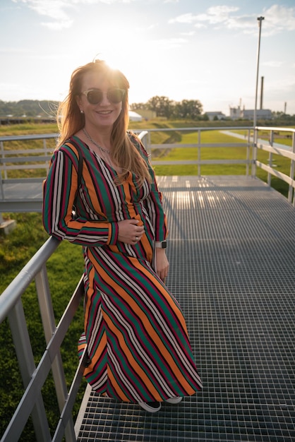 A woman in a striped dress stands on a metal railing.