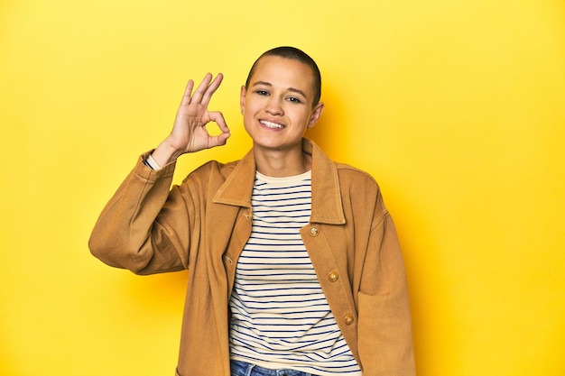 Woman in striped tee and denim shirt yellow backdrop cheerful and confident showing ok gesture