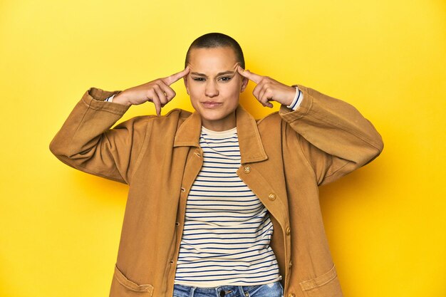 Woman in striped tee and denim shirt yellow backdrop focused on a task